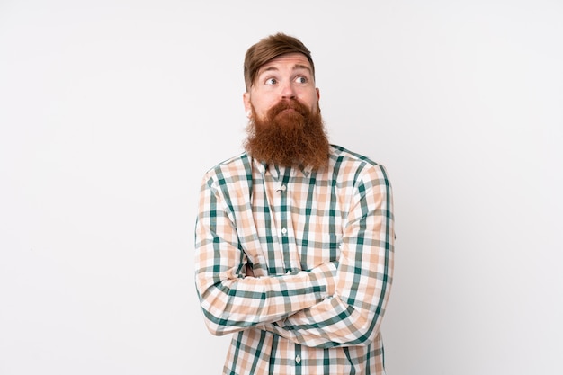 Uomo di redhead con la barba lunga sul muro bianco isolato facendo dubbi gesto mentre si sollevano le spalle