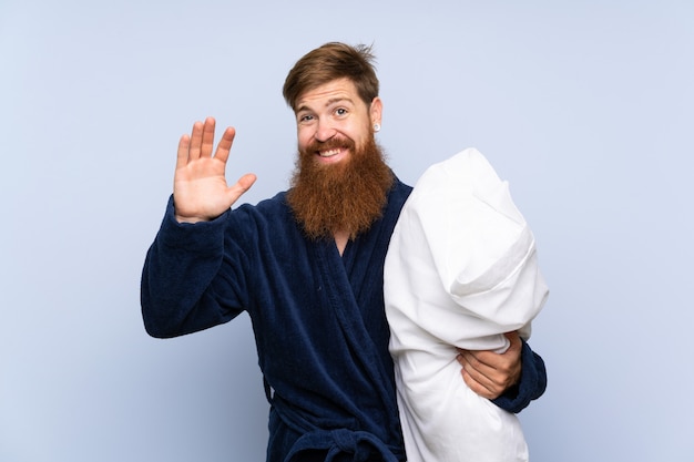 Uomo di redhead in pigiama sopra priorità bassa isolata che saluta con la mano con l'espressione felice