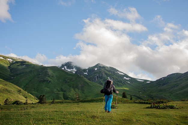 Uomo di retrovisione sulla collina che esamina le montagne rocciose coperte di erba con i resti della neve