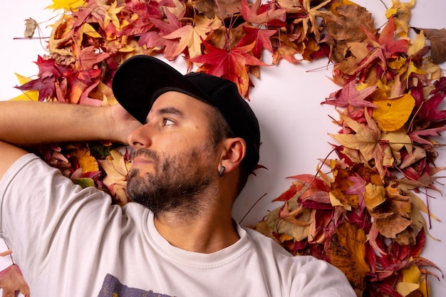 Uomo di sfondo autunnale con un berretto nero in uno studio sdraiato su foglie colorate