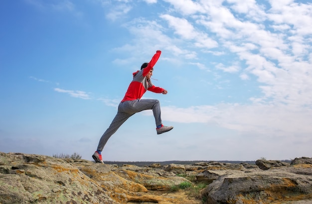 Uomo di sport che corre, salta sopra le rocce nella zona di montagna. Montare l'allenamento del corridore maschile e saltare all'aperto nella splendida natura