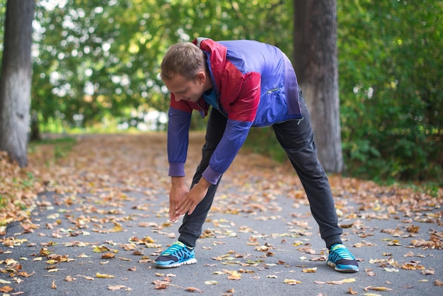 Uomo di sport che si estende al parco autunno facendo esercizi Concetti di fitness