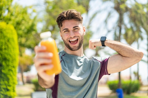 Uomo di sport che tiene un succo d'arancia all'aperto