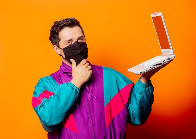 Uomo di stile con maschera e tuta anni '80 con computer notebook