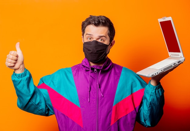 Uomo di stile con maschera e tuta anni '80 con computer notebook