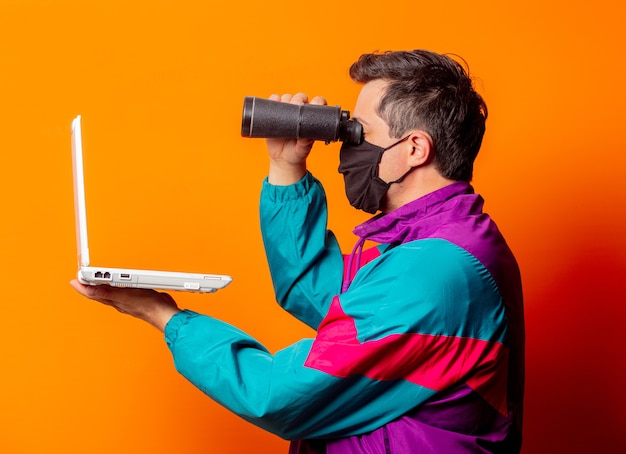 Uomo di stile con maschera e tuta anni '80 con computer portatile e binocolo