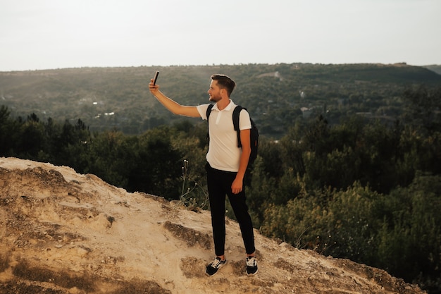 Uomo di viaggio con lo zaino che prende selfie sulla montagna rocciosa.