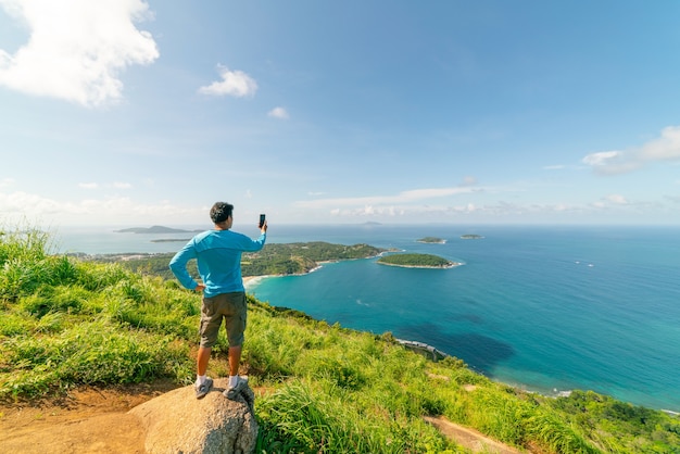 Uomo di viaggio in piedi sulla roccia Scatta una foto o un video vista del paesaggio al punto di vista di Phahindum famoso punto di riferimento a Phuket Thailandia Punto di vista per vedere la spiaggia di Capo Promthep Naiharn e la spiaggia di Yanui Vista incredibile.