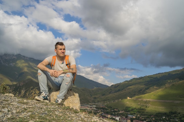 Uomo di viaggio stanco che riposa sulla collina Turista maschio esausto seduto sulla pietra dopo il trekking attivo in montagna