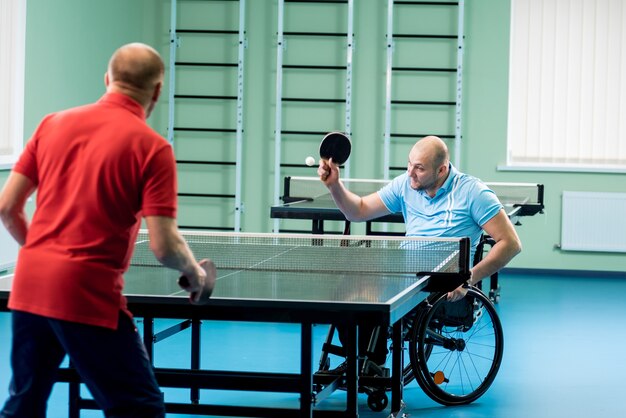 Uomo disabile adulto su sedia a rotelle gioca a ping pong con il suo allenatore