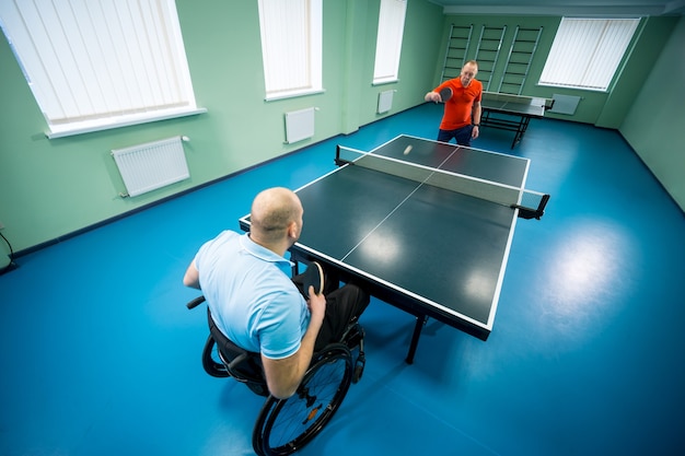 Uomo disabile adulto su sedia a rotelle gioca a ping pong con il suo allenatore