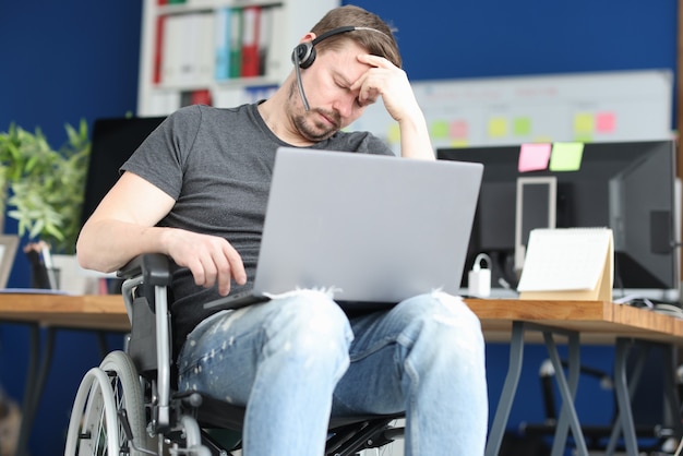 Uomo disabile che dorme in sedia a rotelle con il computer portatile in grembo. Resilienza al concetto di lavoro