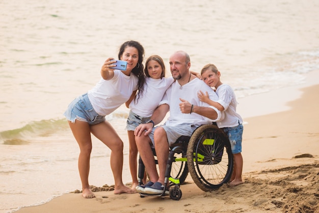 Uomo disabile in sedia a rotelle con la sua famiglia sulla spiaggia.