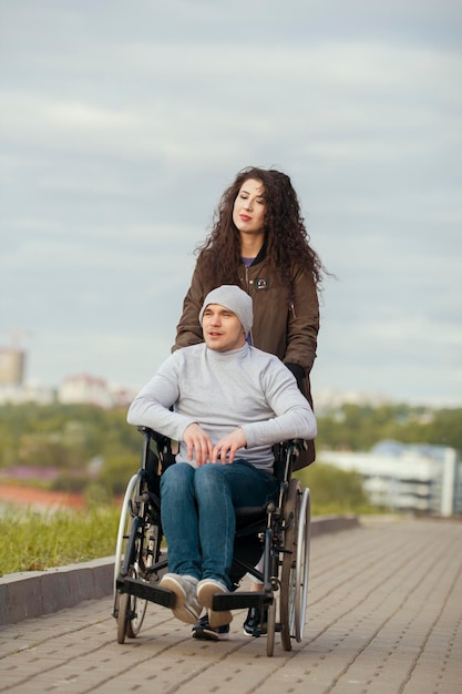 Uomo disabile in sedia a rotelle con una giovane donna che cammina per la strada della città