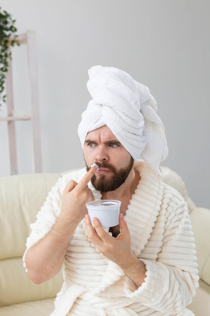 Uomo divertente che applica una crema efficace sulla sua spa per la pelle del viso a casa per il corpo e la cura della pelle per gli uomini