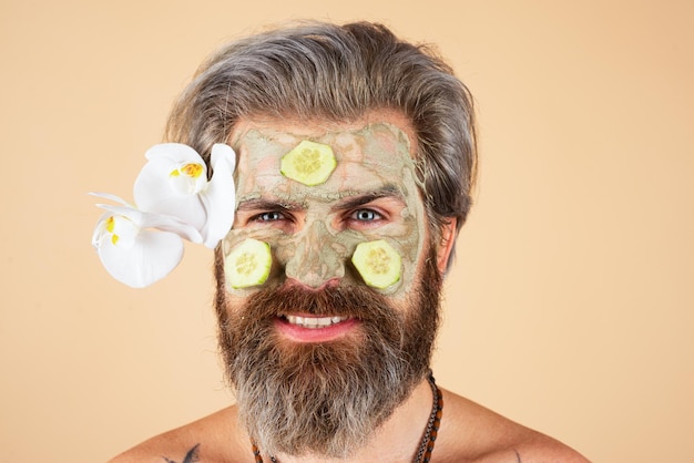 Uomo divertente con fette di cetriolo sul viso. Spa, dermatologia, benessere e concetto di trattamento del viso. Uomo con maschera idratante cosmetica, sfondo per studio isolato. Cura del viso maschile.