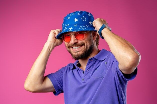 Uomo divertente di smiley barbuto che indossa cappello da spiaggia e occhiali da sole contro il rosa