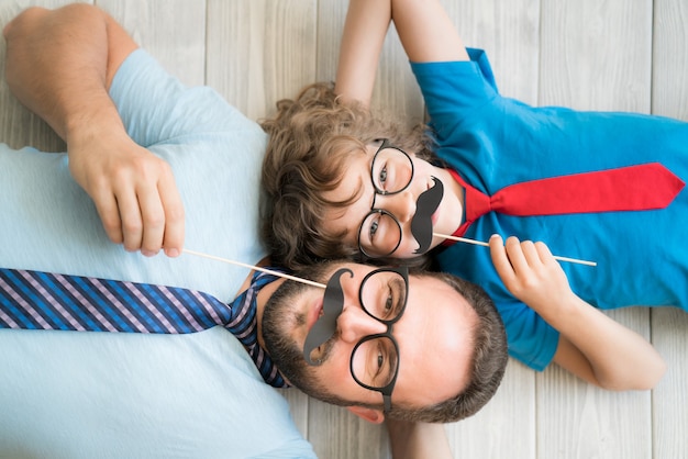 Uomo divertente e bambino con baffi finti. Famiglia felice che gioca in casa