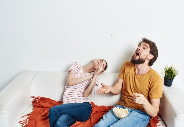 Uomo divertente e donna energica che guarda la TV sul divano popcorn in una comunicazione di famiglia del piatto