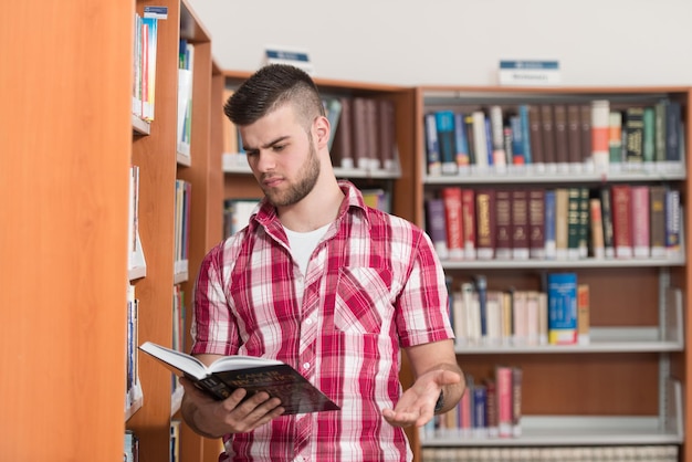 Uomo divertente e pazzo che legge dal libro in biblioteca