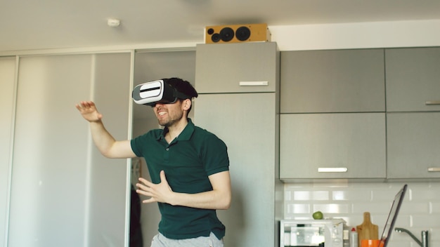 Uomo divertente in cuffia per realtà virtuale che balla in cucina al mattino mentre si ascolta la musica