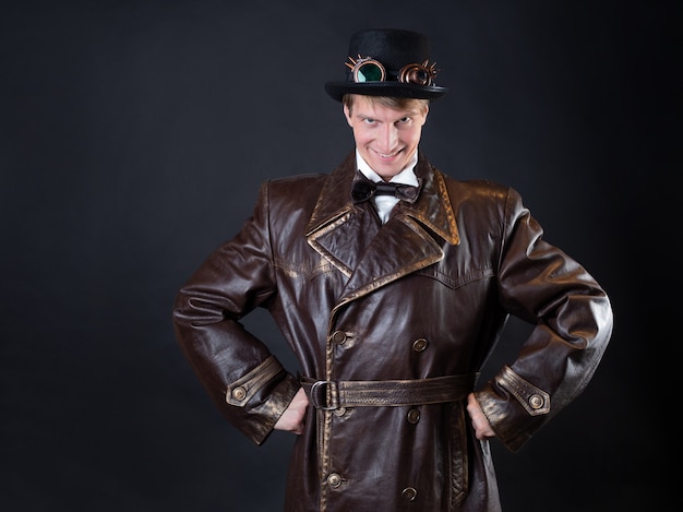 Uomo divertente in un ridicolo cappotto di pelle e un cappello a cilindro, stile vintage di abbigliamento, foto su sfondo nero, un personaggio scherzoso fa facce stupide