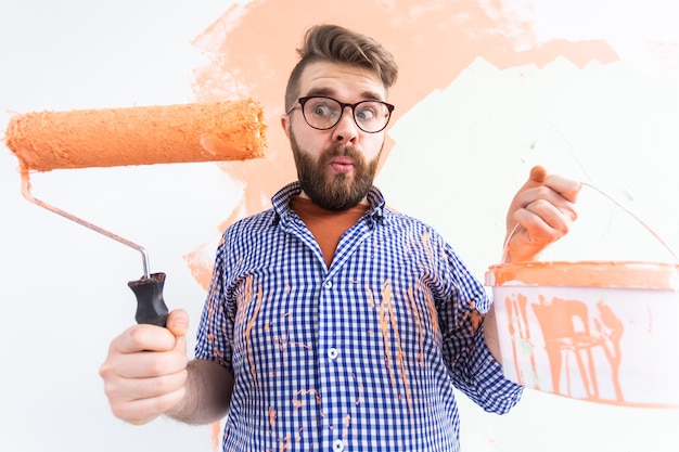 Uomo divertente pittura parete interna con rullo di vernice nella nuova casa. Ragazzo con il rullo che applica la vernice su un
