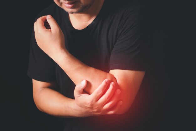 Uomo dolore al gomito Il focolare è evidenziato in rosso Close Up Uomo che sente un dolore al gomto su sfondo nero Sindrome del tunnel carpale artrite concetto di malattia neurologica