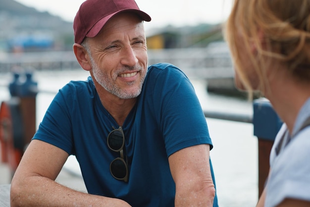 Uomo donna e porto con felice conversazione in vacanza di viaggio o appuntamento sull'oceano sotto il sole estivo Coppia senior parla e ascolta con cura legame romantico o amore via mare per vacanze all'aperto