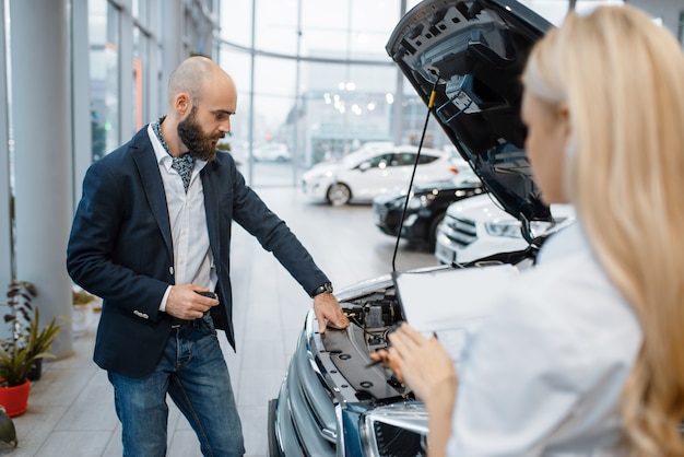 Uomo e commessa che scelgono l'auto nella concessionaria auto. Cliente e venditore nello showroom del veicolo, persona di sesso maschile che acquista il trasporto, attività di rivenditore di automobili