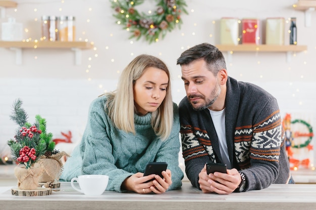 Uomo e donna a casa che guardano i telefoni cellulari trascorrono del tempo sui social network, Natale e Capodanno