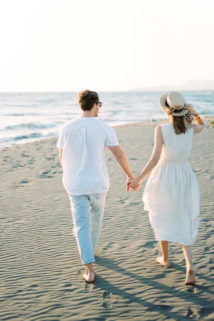 Uomo e donna a piedi nudi che camminano lungo la spiaggia tenendosi per mano