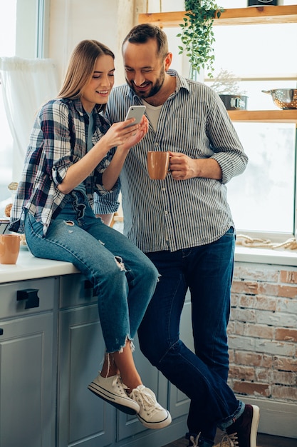 Uomo e donna allegri in cucina che sorridono e guardano lo smartphone