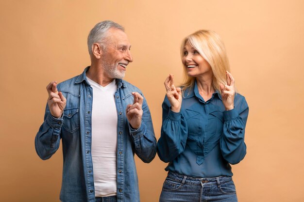 Uomo e donna anziani felici che incrociano le dita sullo sfondo beige