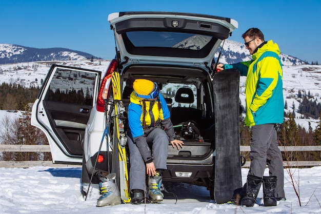 Uomo e donna che si vestono con attrezzatura da sci vicino a un'auto suv. montagne sullo sfondo