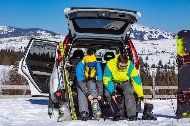 Uomo e donna che si vestono con attrezzatura da sci vicino a un'auto suv. montagne sullo sfondo