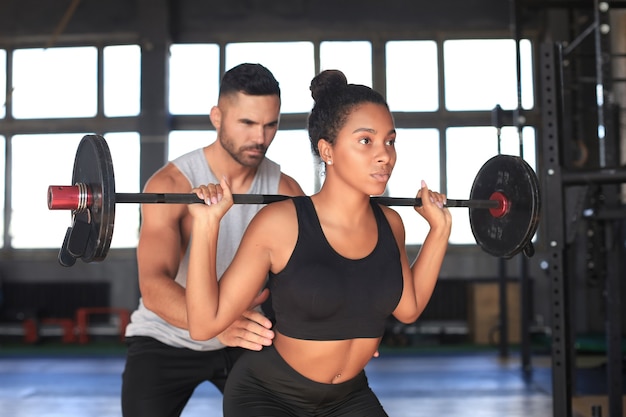 Uomo e donna con bilanciere che flette i muscoli in palestra.