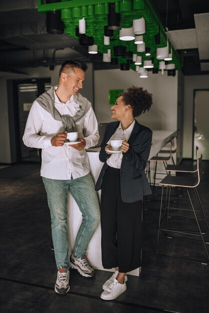 Uomo e donna con caffè in piedi sorridente in ufficio