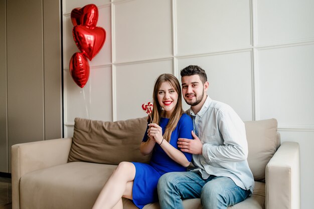 Uomo e donna con lecca-lecca caramelle a casa sul divano con palloncini a forma di cuore