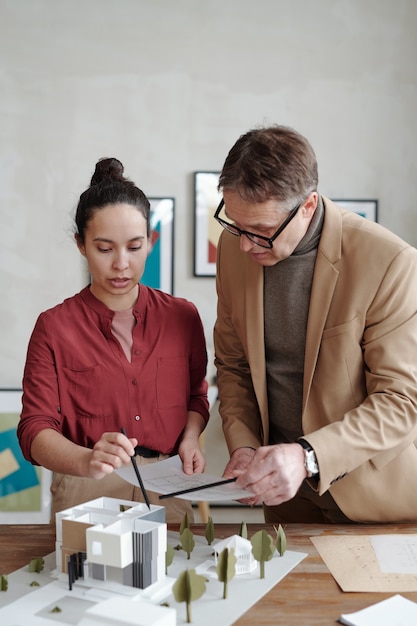 Uomo e donna concentrati che tengono il piano della casa e lo confrontano con il modello 3D della casa mentre lavorano al progetto architettonico