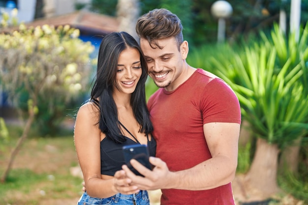 Uomo e donna coppia sorridente fiducioso utilizzando smartphone al parco