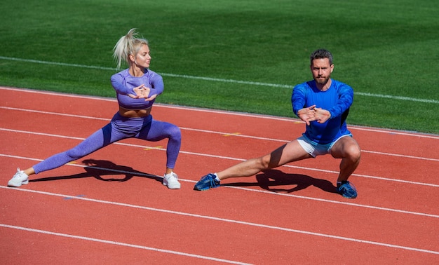 Uomo e donna di sport fitness che si scaldano e si allungano insieme sulla pista dello stadio all'aperto indossando abbigliamento sportivo, allenatore.