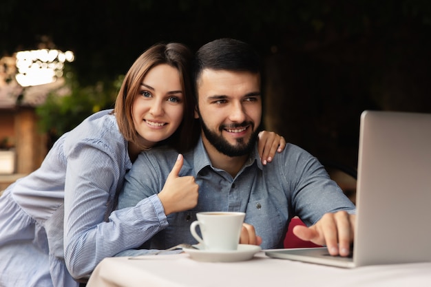 Uomo e donna felici che lavorano da casa, giovane coppia con la tazza di caffè che lavora al computer portatile all'interno
