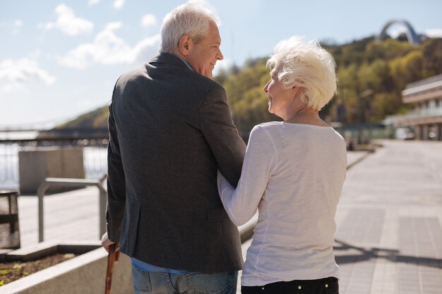 Uomo e donna in pensione calmi incoraggiati che percorrono la strada insieme divertendosi e sorridendo