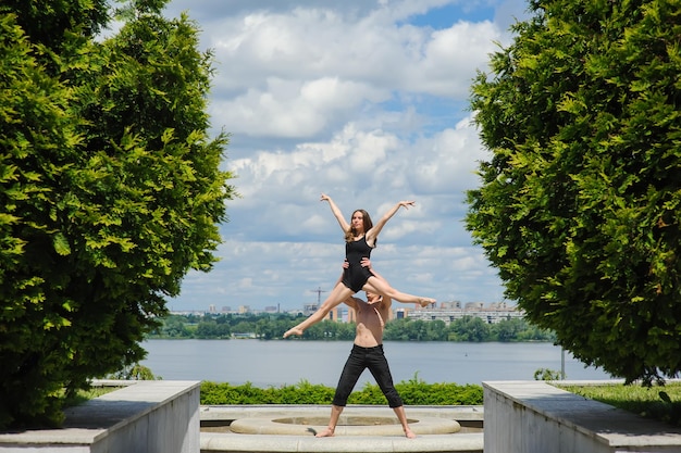 Uomo e donna in posa di danza appassionata nel parco Giovane coppia che balla danza moderna all'aperto Uomo con torso nudo Uomo che solleva la donna sopra la testa Cielo e acqua fiume sullo sfondo