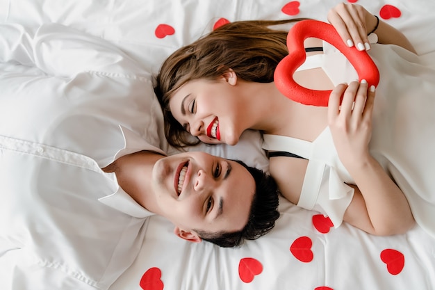 Uomo e donna innamorata a letto con coriandoli a forma di cuore