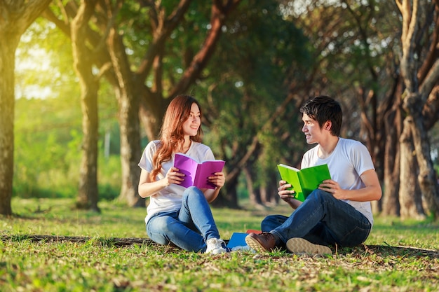 uomo e donna seduti e leggendo un libro nel parco