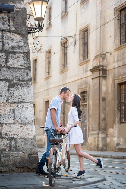 Uomo e donna sono attratti l'uno dall'altro che si baciano vicino alla bici tandem retrò in un ambiente urbano nelle strette stradine