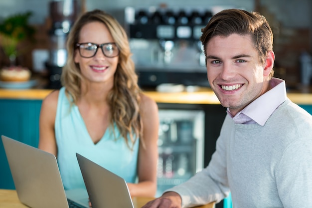 Uomo e donna sorridenti che utilizza computer portatile nel caffè