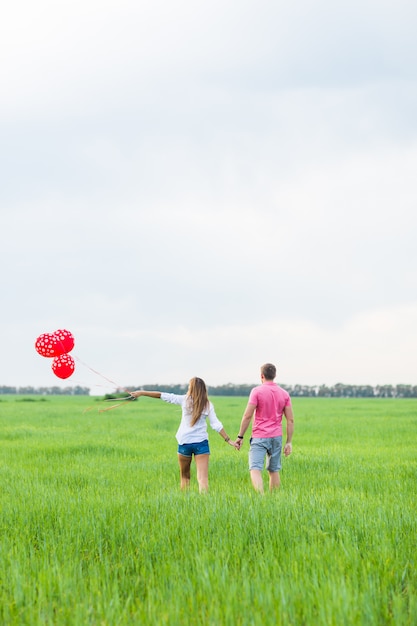 Uomo e donna sul campo con palloncini rossi. Coppie felici sulla vista posteriore della natura